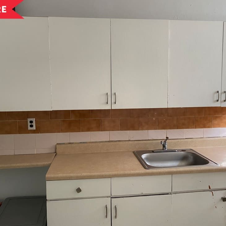 an empty kitchen with white cabinets and brown tile on the walls, including a stainless steel sink