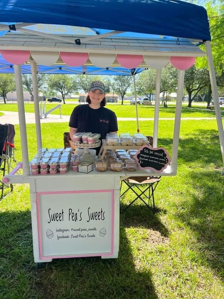 a person standing behind a table with food on it in the grass at a park