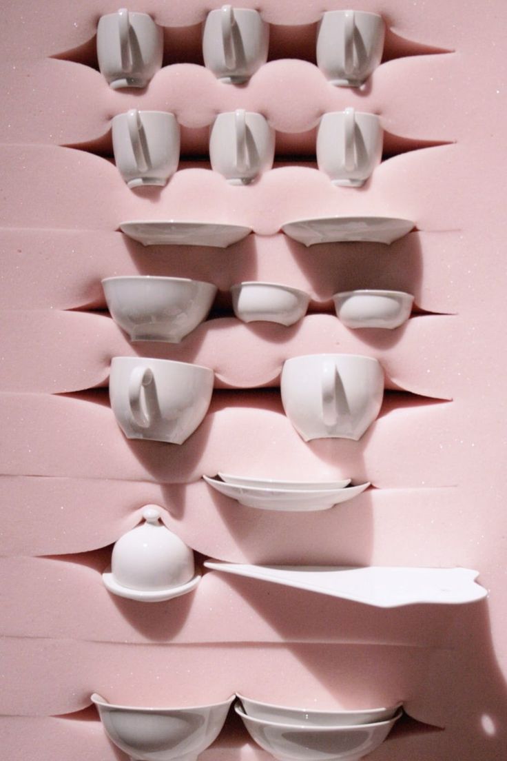 several white bowls and plates are arranged on a pink wall