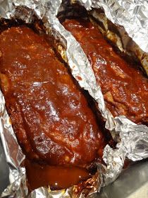 two pieces of meat covered in tin foil on top of a table with sauce and ketchup