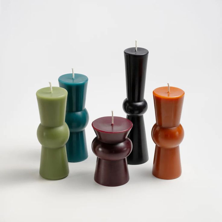 several different colored candles sitting next to each other on a white surface with one candle in the middle