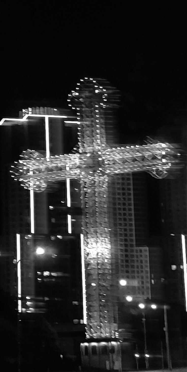 a black and white photo of a large cross in the middle of a city at night