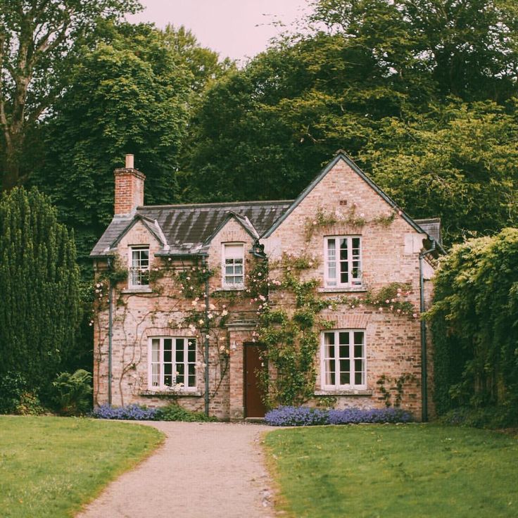 an old brick house surrounded by greenery and trees in the country side with a path leading to it