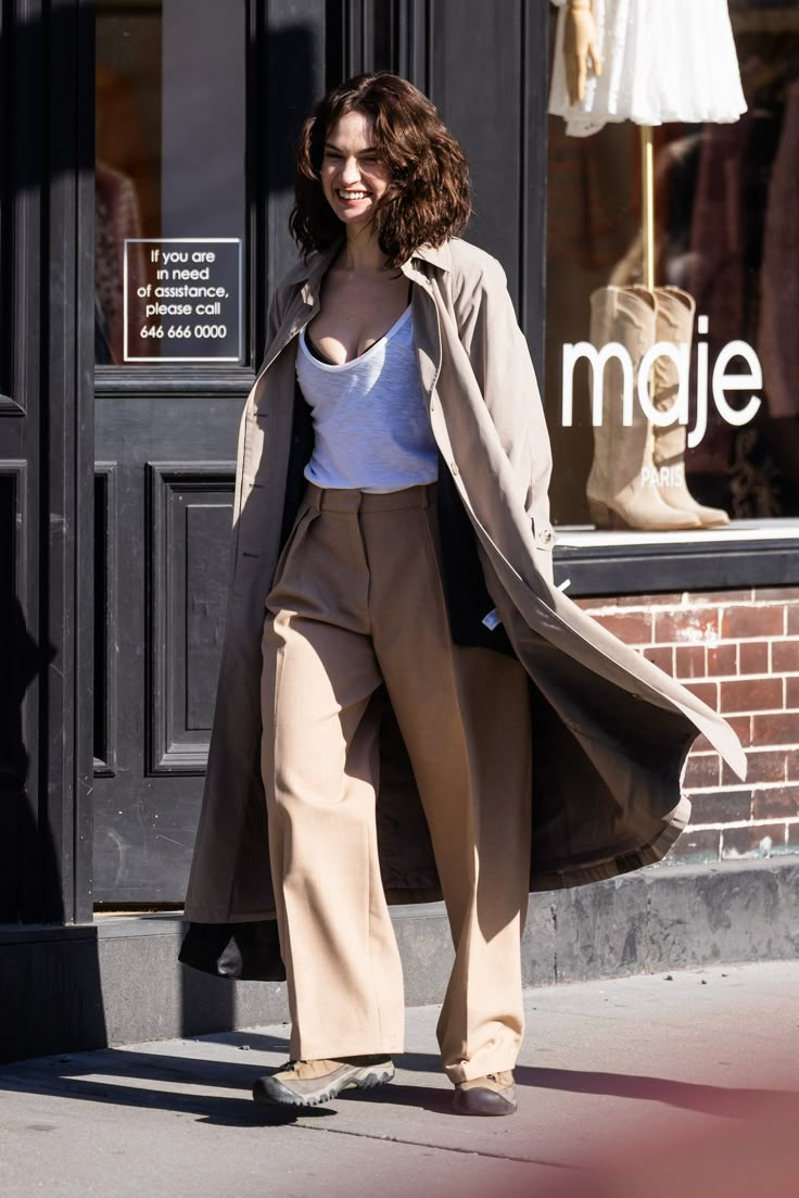 a woman is walking down the street in her pants and trench coat while wearing high heels