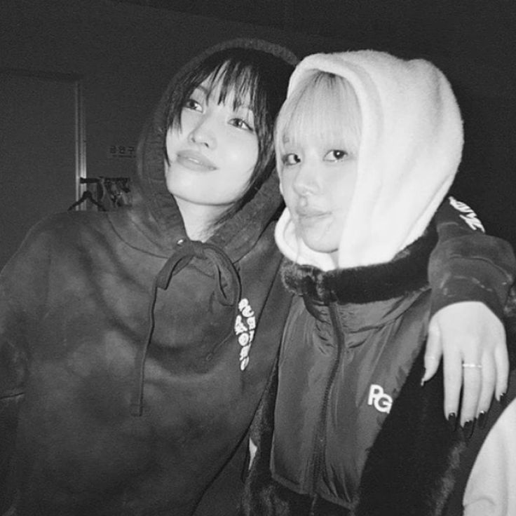 two young women standing next to each other in black and white photo, one wearing a hoodie