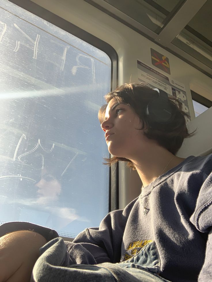 a woman sitting in the back seat of a bus looking out the window with headphones on