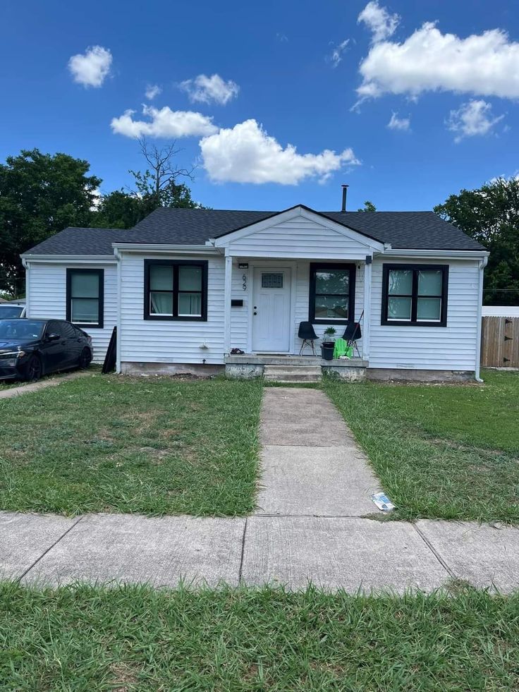 a small white house sitting on the side of a road with cars parked in front of it