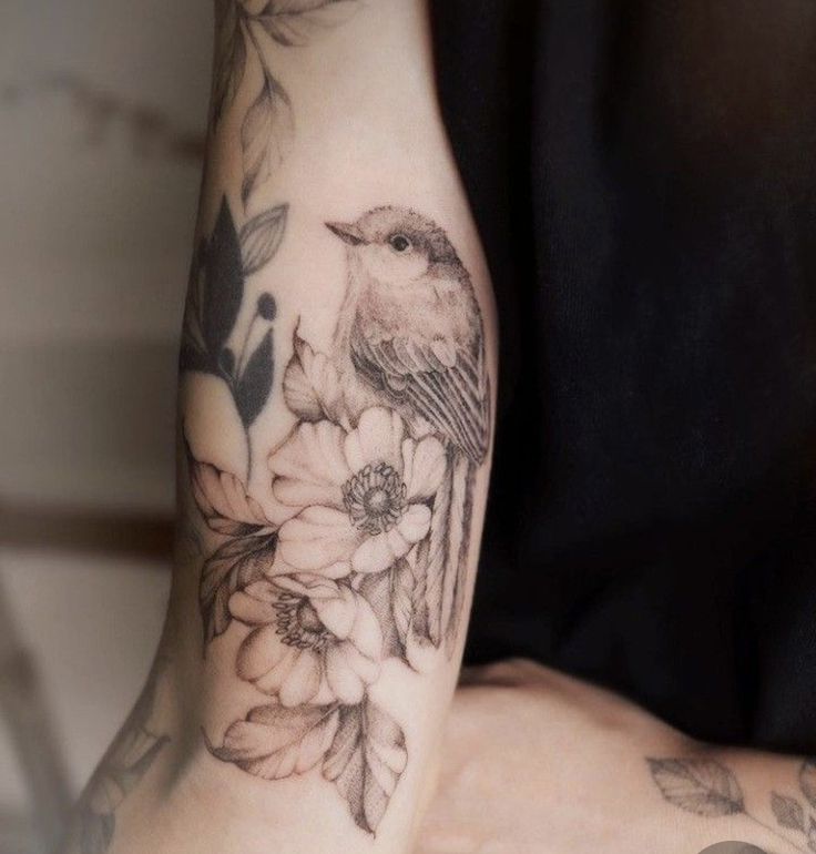 a woman's arm with flowers and a bird tattoo on the left side of her arm