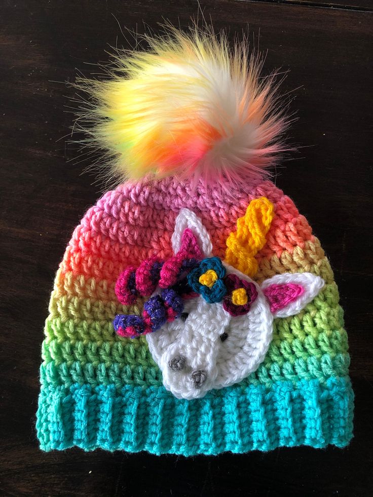 a crocheted hat with a unicorn on it and a multicolored pom - pom