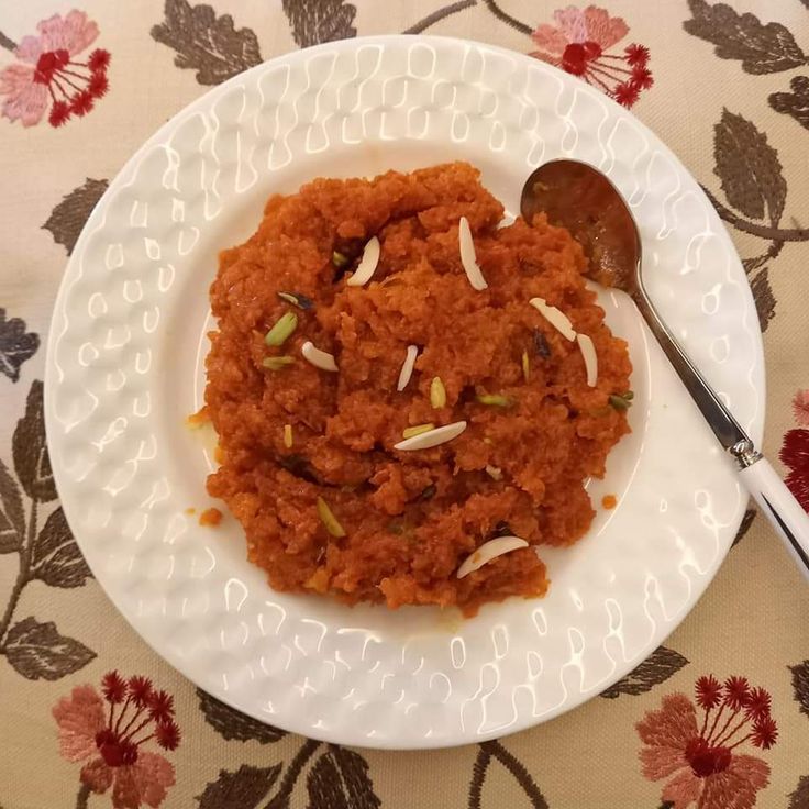 a white plate topped with food on top of a flower covered table cloth next to a spoon