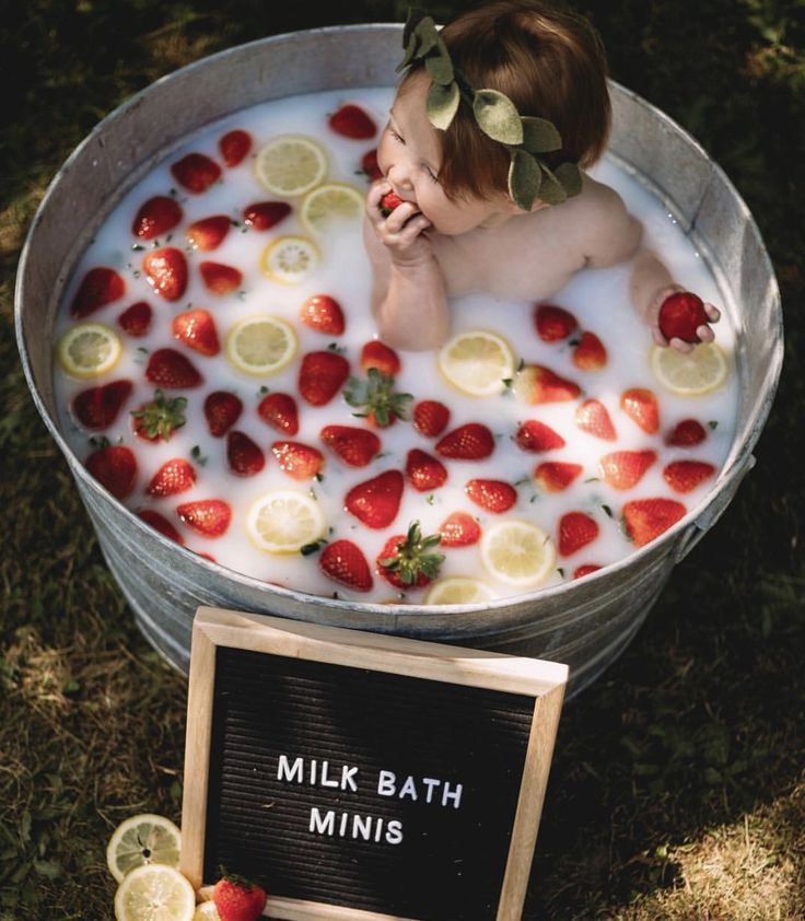 a baby sitting in a tub filled with milk and strawberries next to a sign that says milk bath minis