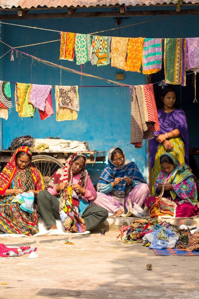 several women sitting on the ground in front of a blue building with clothes hanging from it