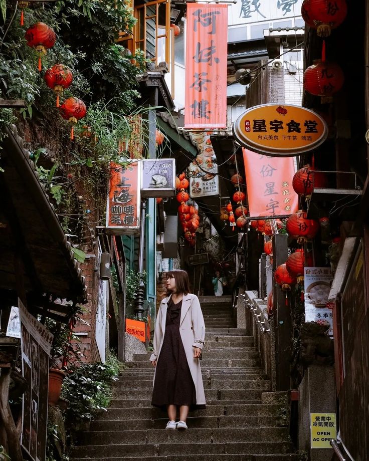 a woman standing on the steps in an alley way with lanterns hanging above her head