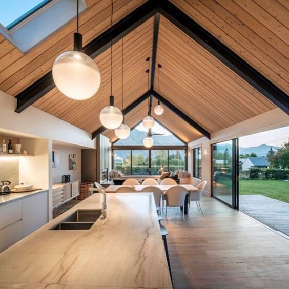 an open kitchen and dining area with wood ceilinging, large windows, and modern lighting fixtures