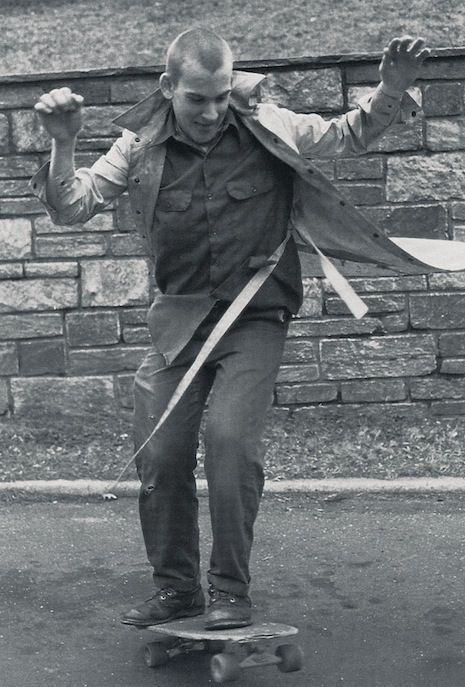 a man riding a skateboard down a street next to a brick wall and holding two swords