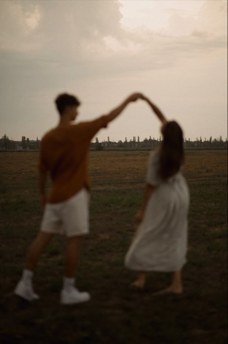 two people standing in a field holding hands with the sky behind them and one person flying a kite