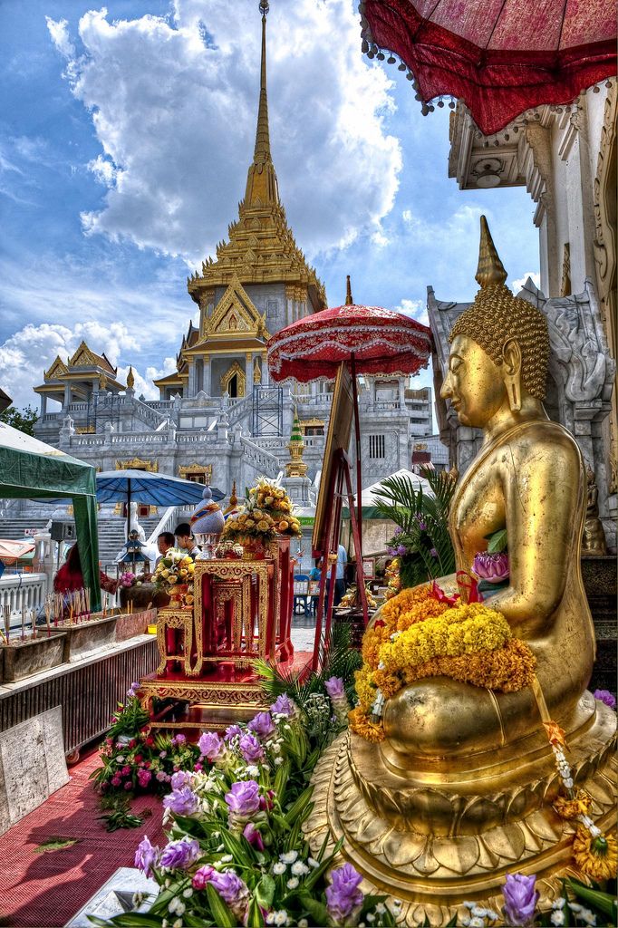 a golden buddha statue sitting under an umbrella in front of a building with many flowers