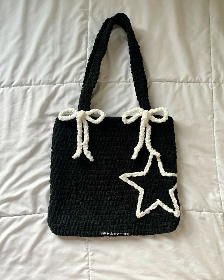 a crocheted black bag with white stars on the front and bottom, sitting on a bed