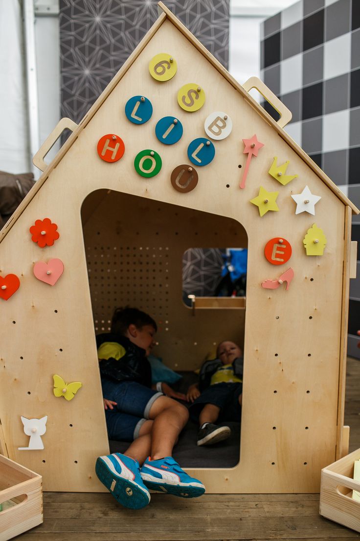 two children are sitting in a wooden house with magnets on the walls and doors