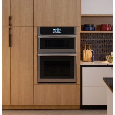 two ovens side by side in a kitchen with wooden cabinets and counter tops on either side