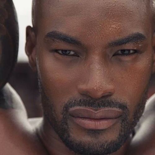 a close up of a man with tattoos on his arm and chest, looking at the camera