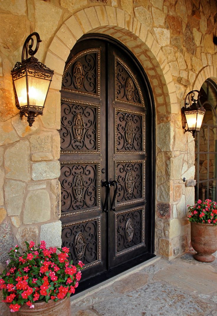 an ornate iron door with flower pots and two lights on the side of the building