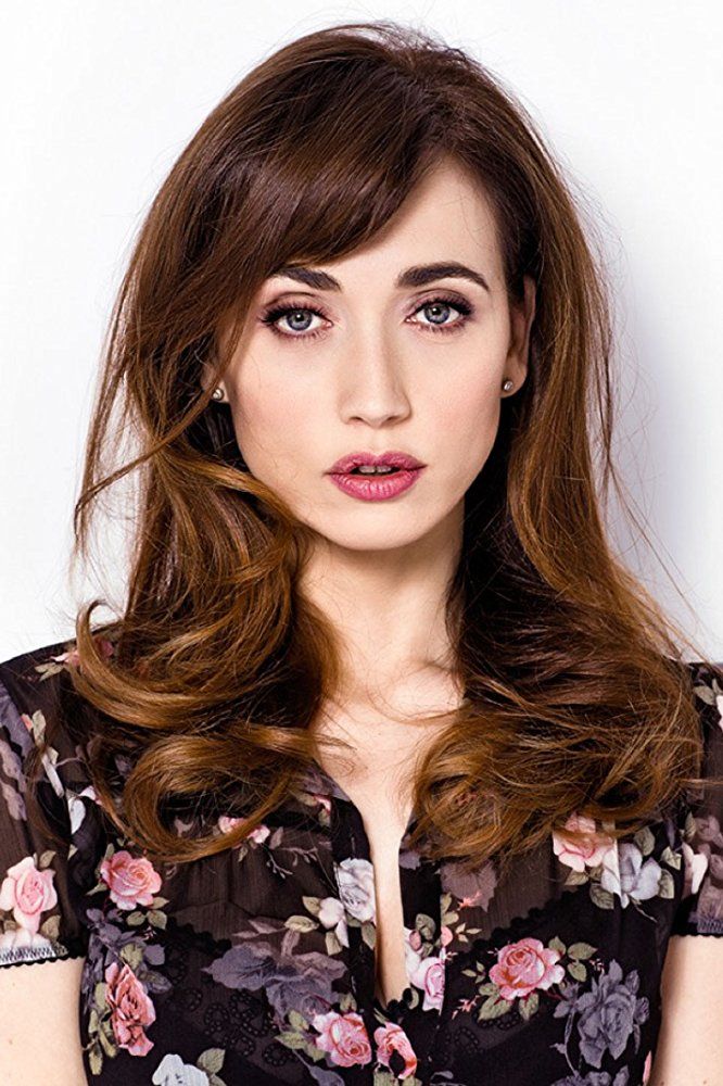 a woman with long brown hair wearing a black floral shirt and posing for the camera