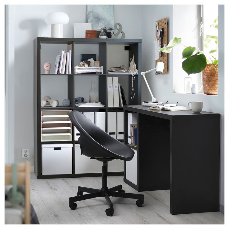 a black chair sitting in front of a desk with bookshelf and shelves behind it