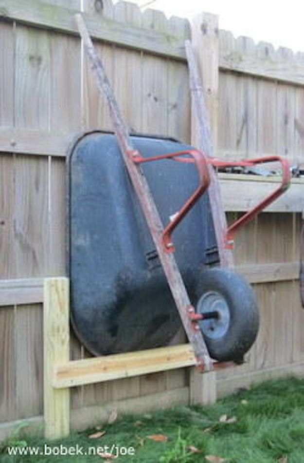 a wheelbarrow attached to the side of a wooden fence next to a lawn mower