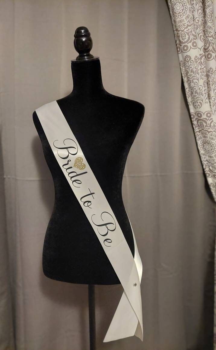 "This bridal sash is made with 3 inch soft satin and has \"Bride to Be\" in black letters.  Complimented with a unique gold heart with a cluster of hearts inside. The Sash is 72 inches in length and comes with a crystal pin to secure the Sash in place. This sash is perfect for a bridal shower, wedding party, or a bachelorette party." Bride Sash Bachelorette, Sash Bachelorette, Bride Sash, Bridal Shower Sash, Gold Sash, Bachelorette Sash, Bride To Be Sash, Bride Shower, Wedding Sash Belt