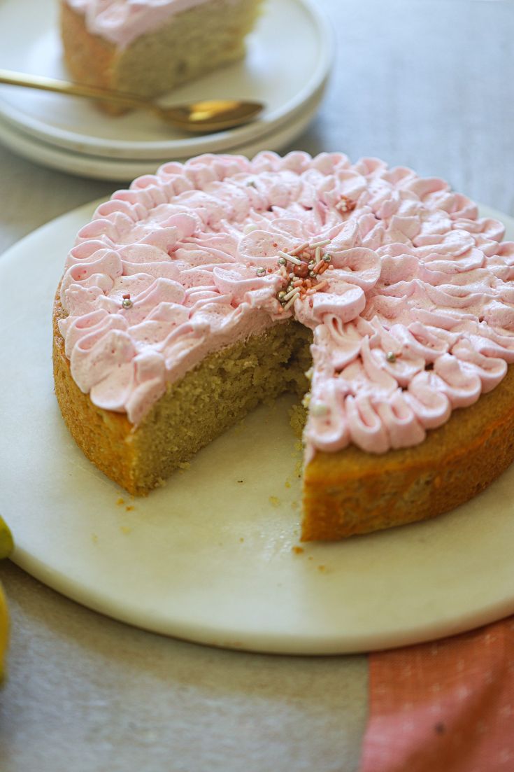 a cake with pink frosting is on a white plate next to two slices of lemons