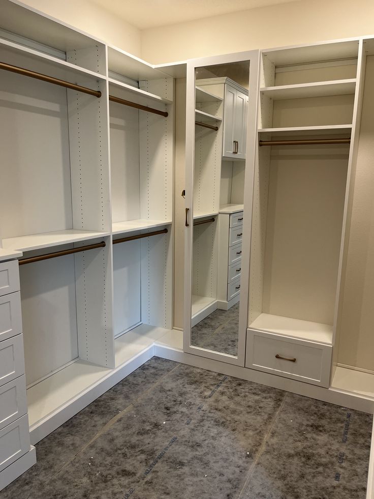 an empty walk in closet with white cabinets and drawers on the walls, carpeted floor