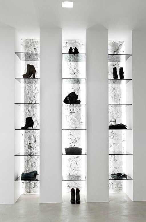 several glass shelves with shoes on them in a room filled with white walls and flooring