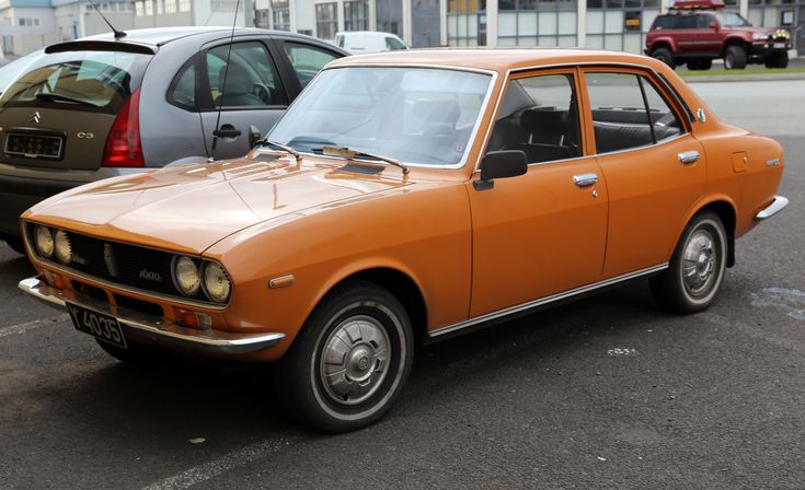 an orange car parked in a parking lot next to other cars