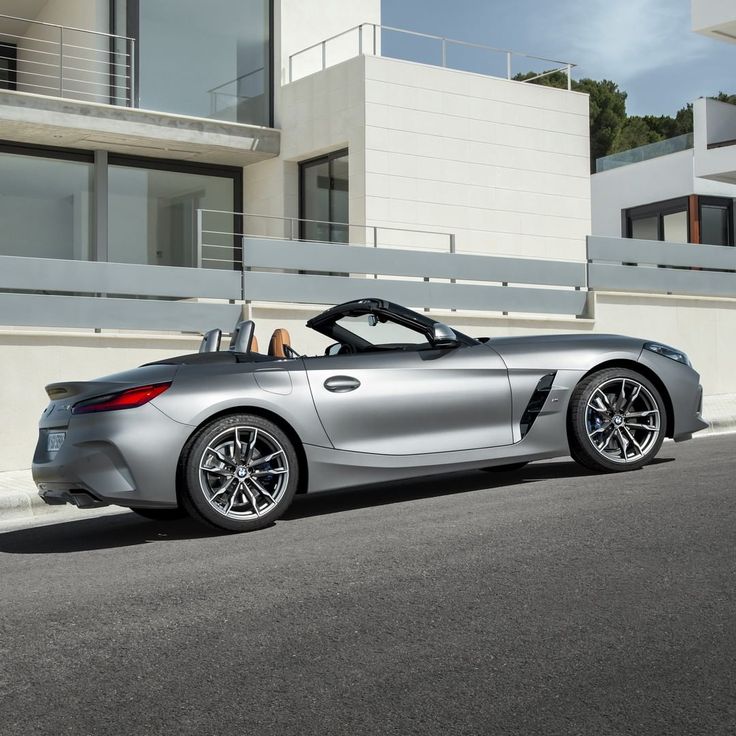 a silver sports car is parked in front of a white building with balconies