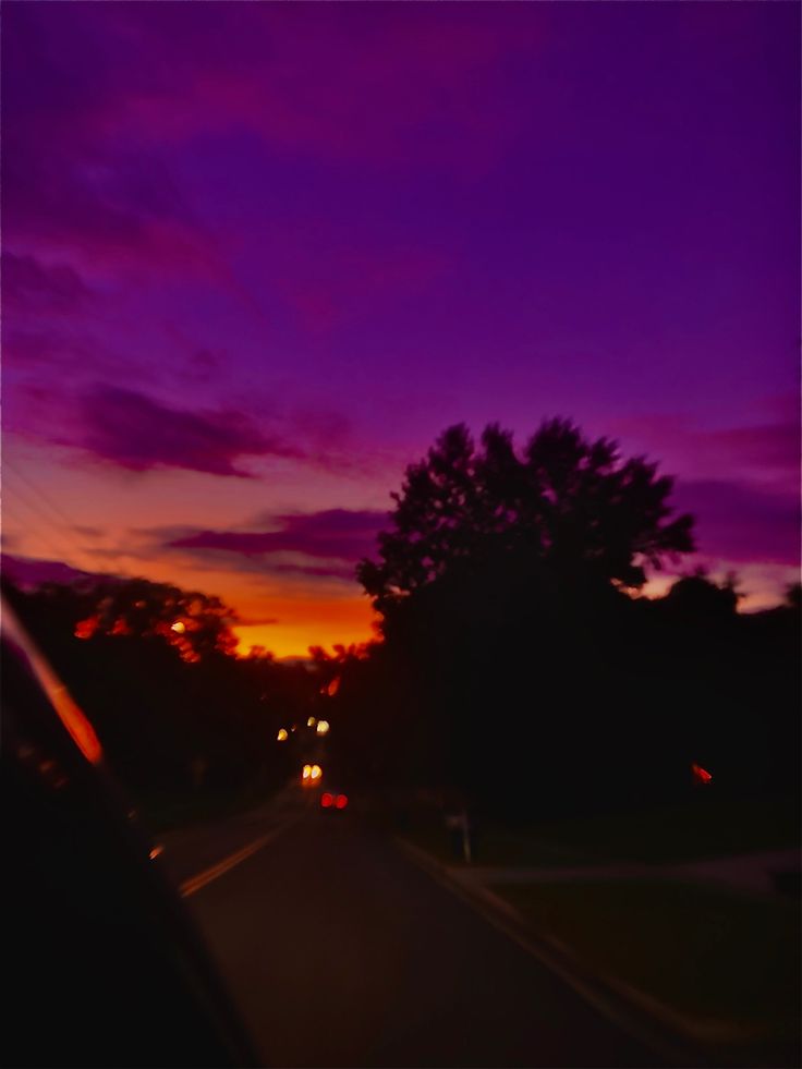 the sun is setting behind some trees and cars on the road in front of them