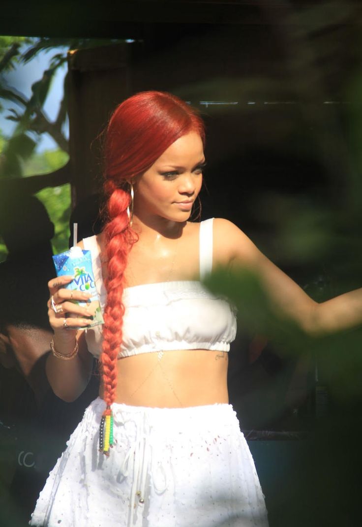 a woman with red hair is holding a drink and looking at her cell phone while wearing a white crop top