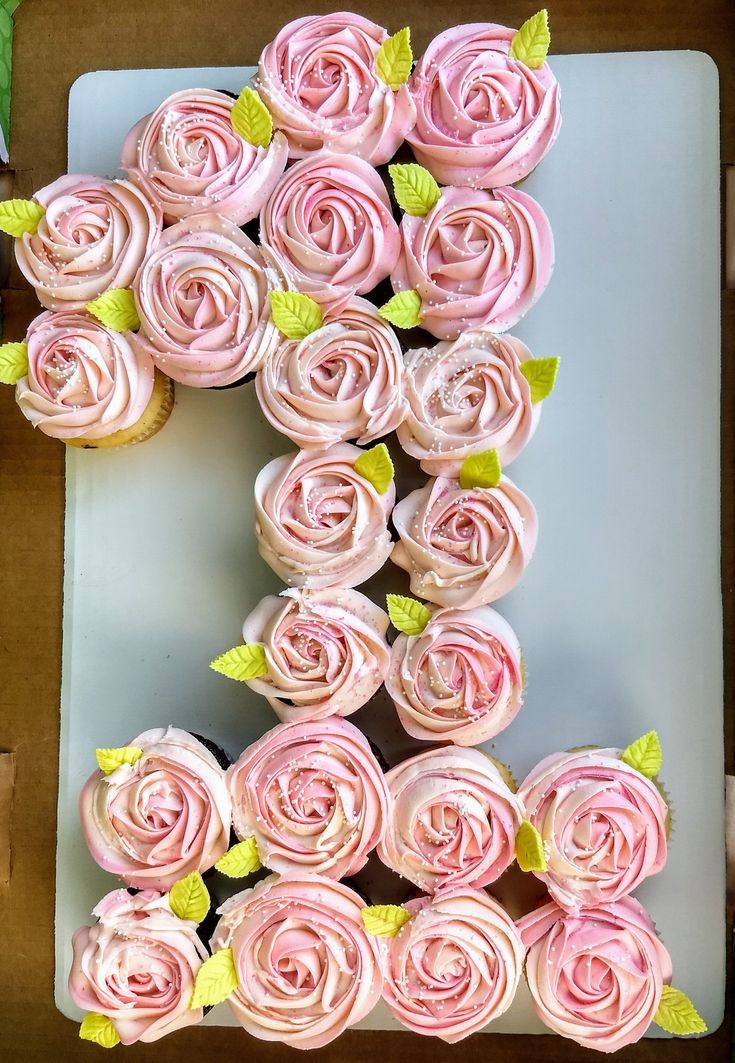 there is a letter made out of cupcakes with pink frosting and green leaves