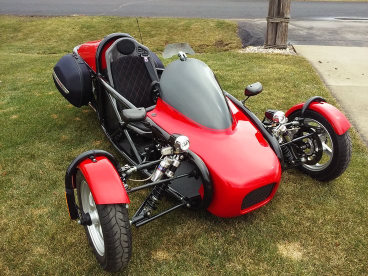 a red three wheeled motorcycle parked in the grass