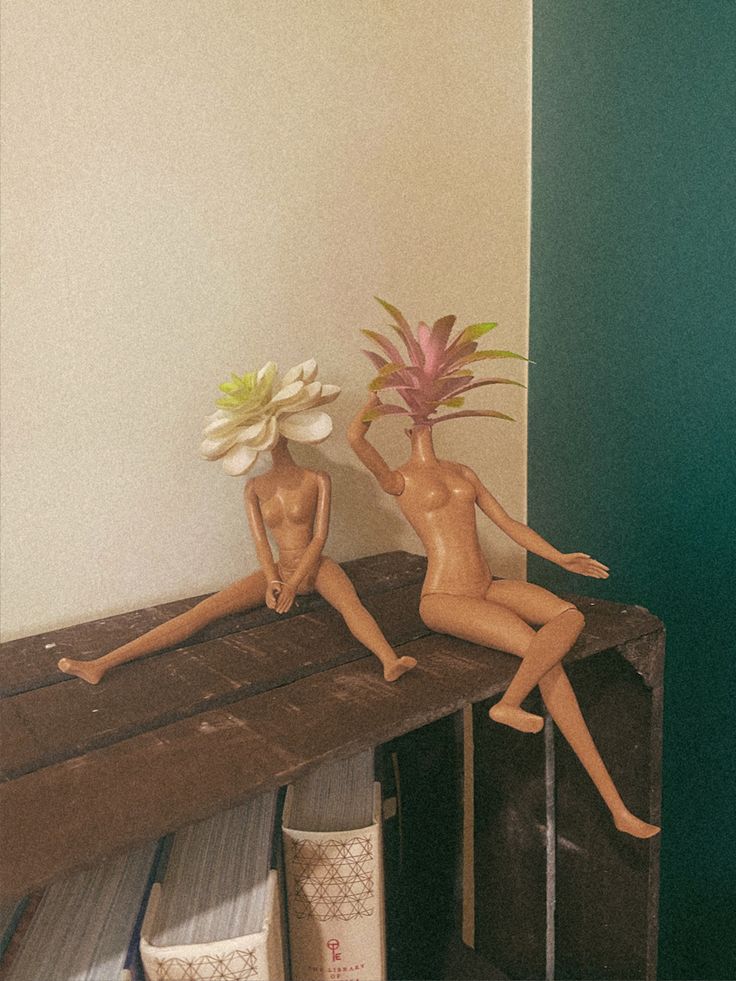 two naked dolls sitting on top of a wooden table with flowers in vases next to them