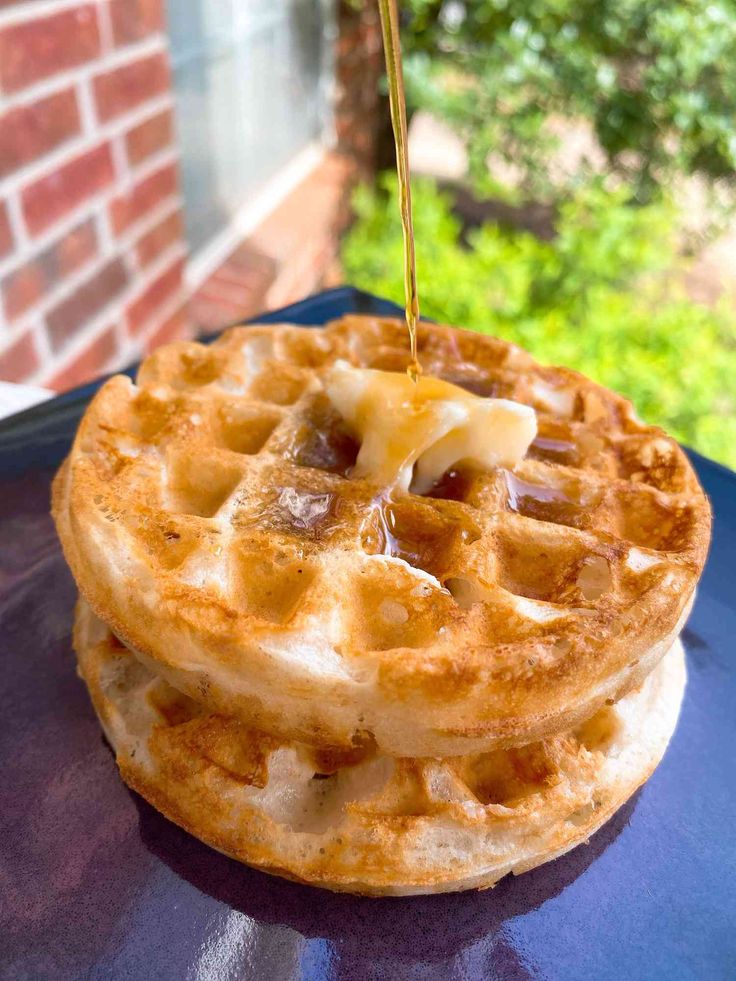 a stack of waffles with syrup being drizzled over them on a blue plate