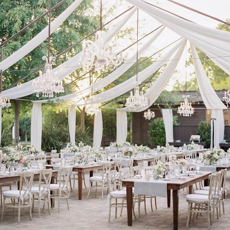 an outdoor wedding reception with white drapes and chandeliers hanging from the ceiling