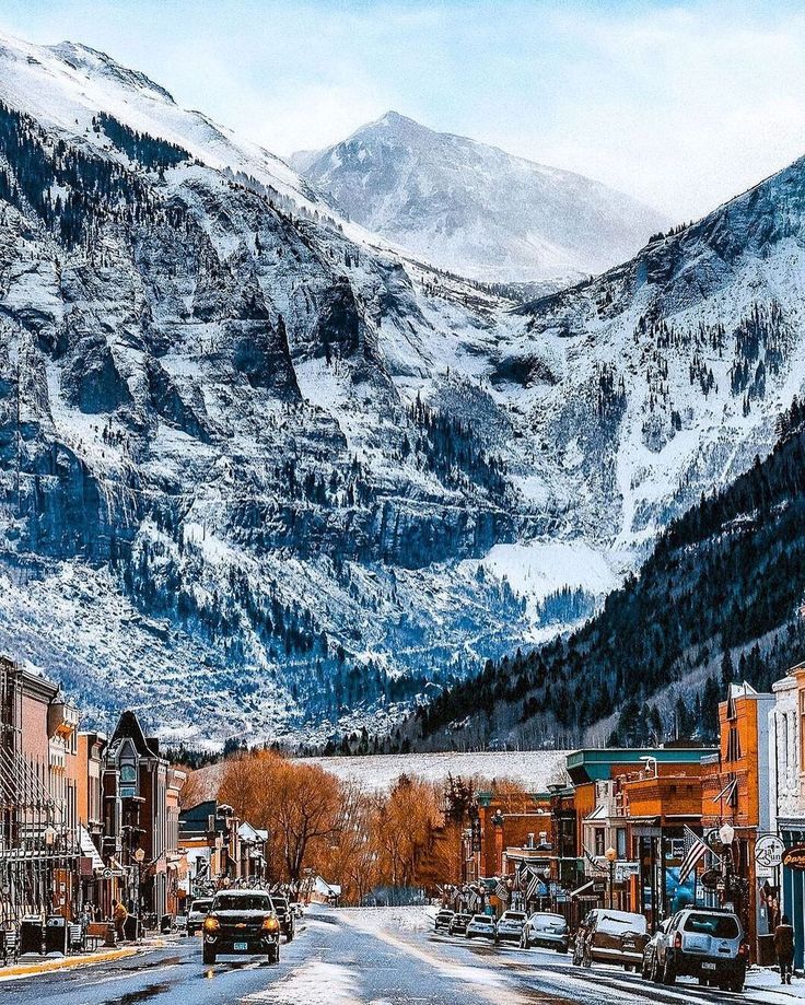 the mountains are covered in snow as cars drive down the road on a snowy day