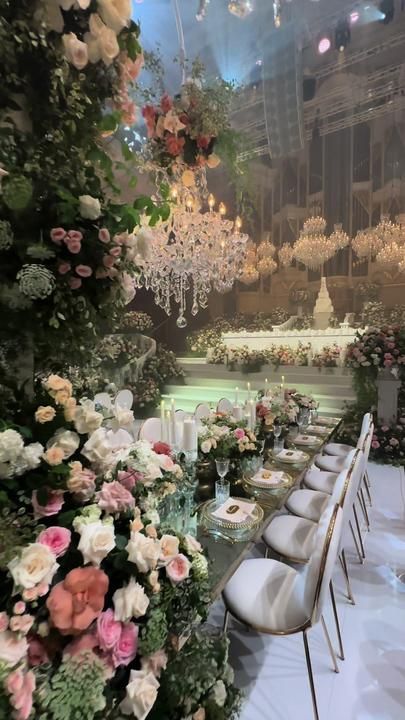 a table set up for a formal dinner with flowers and chandeliers hanging from the ceiling