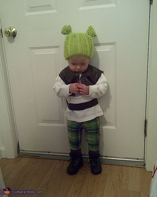 a little boy standing in front of a door wearing a knitted hat and green plaid pants