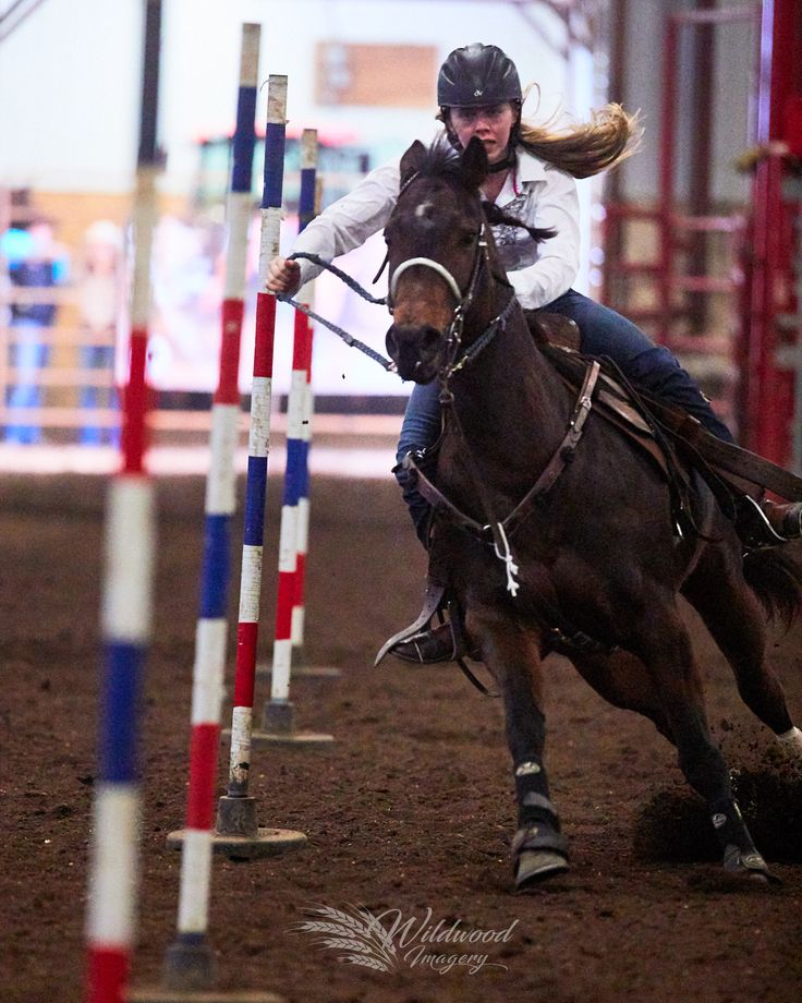 a woman riding on the back of a brown horse over an obstacle in a dirt field