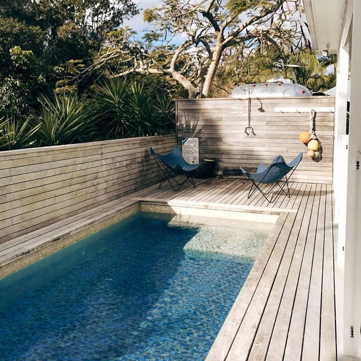 a small pool in the middle of a wooden decked area with chairs and trees