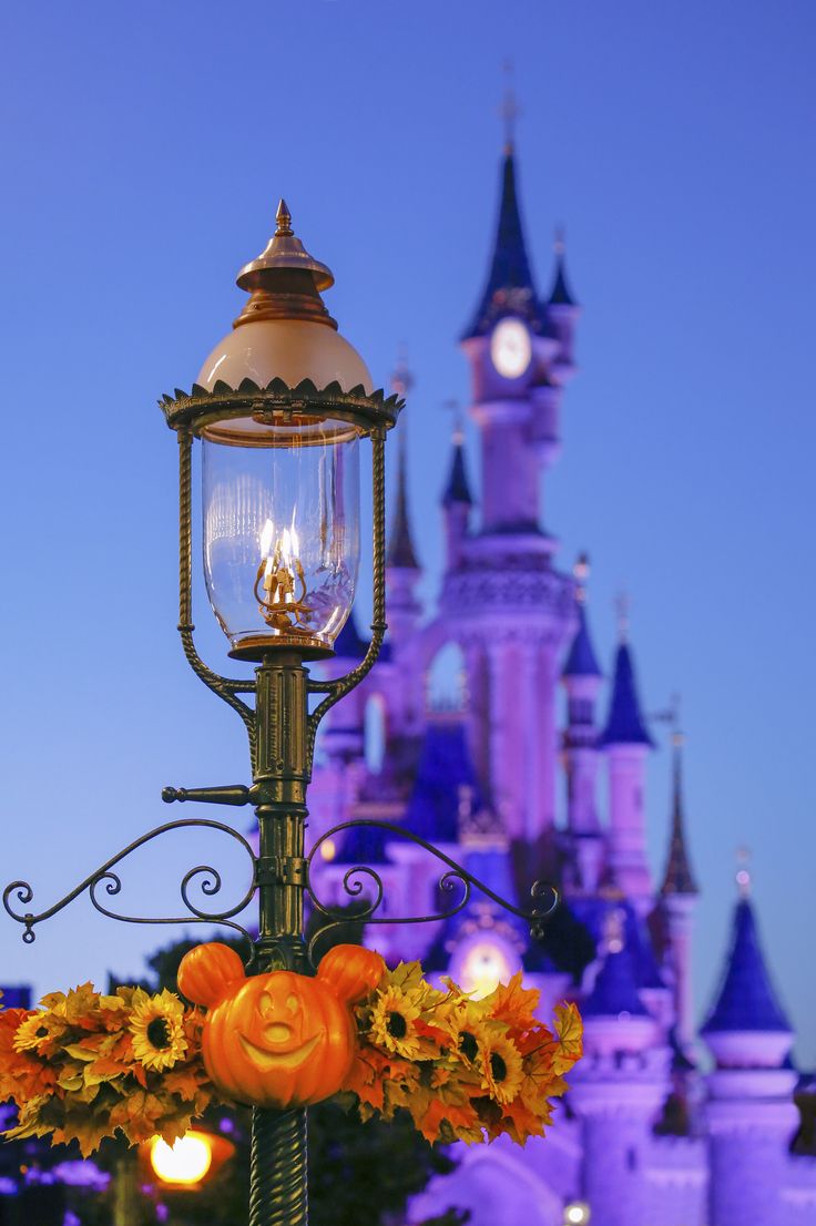 a lamp post with pumpkins and sunflowers on it in front of a castle