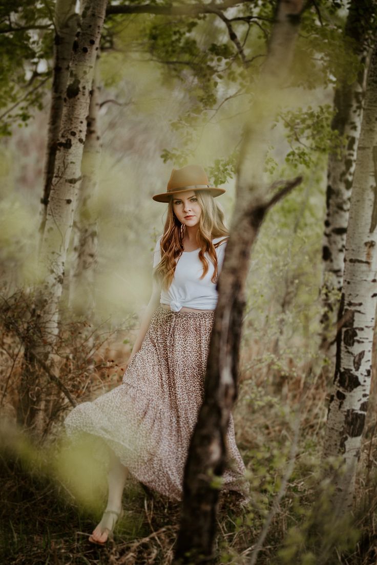 a woman wearing a hat and dress in the woods