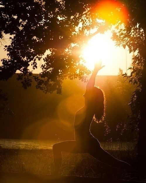 the woman is doing yoga outside in the sun light, with her arms up to the sky